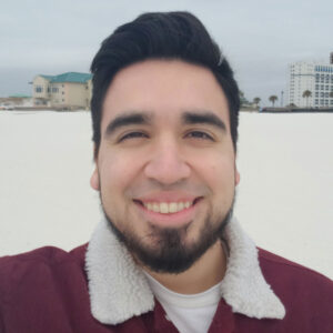 Photo of Christopher in a maroon corduroy jacket on a Florida beach